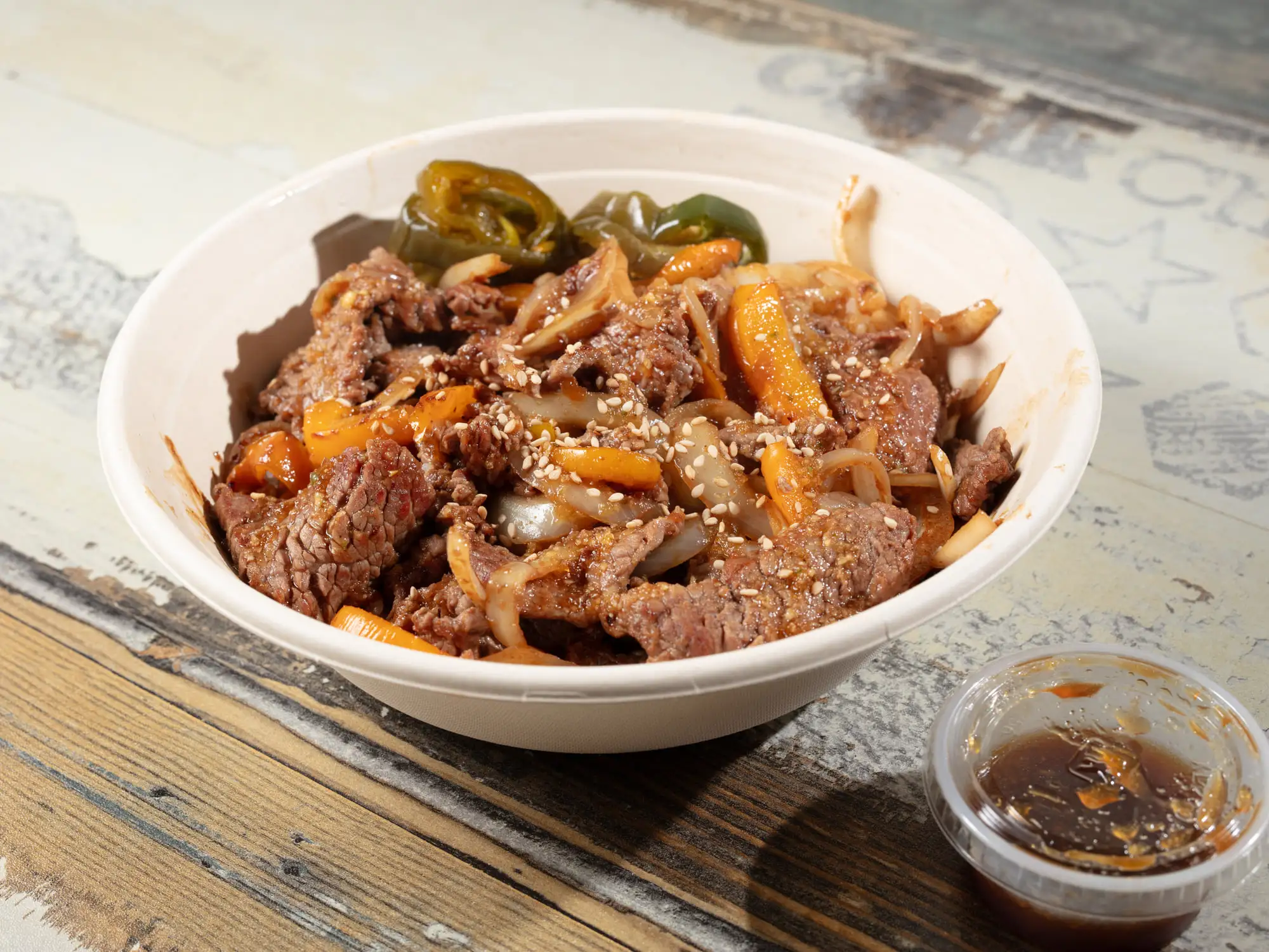 Thin-sliced marinated bulgogi beef with onion and carrot in a white bowl, sesame seeds and blistered green jalapenos on top